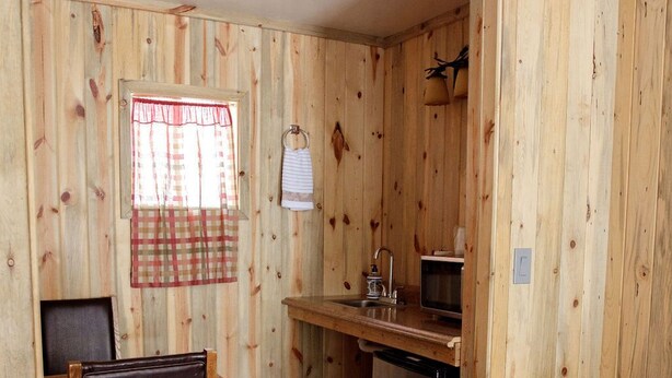 A compact kitchen with wooden walls, a dining area with a chair, and a refrigerator.