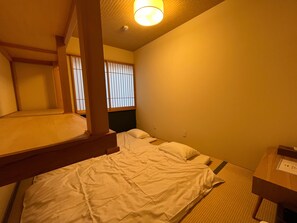 A hotel room with a bunk bed, a desk with a chair, and a window with vertical blinds. - SHUBOU TAMAJIMAN - Hostel (Fussa)