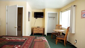 Un dormitorio con cama, escritorio, silla, televisión y ventana con cortinas.