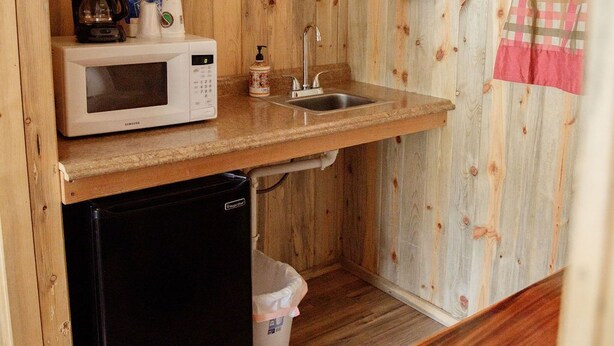 Une cuisine compacte avec des murs en bois, un four à micro-ondes, une machine à café, un évier et un petit réfrigérateur.