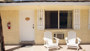 Il s’agit d’un bâtiment d’un seul étage, à la façade beige, avec une porte blanche et une fenêtre dotée de volets. On peut y voir deux chaises Adirondack blanches à l’extérieur.