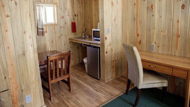 A compact room with a wooden interior, a small desk with a chair, a microwave, and a trash bin. - 0131) Candy Suite 131 (Sevier)