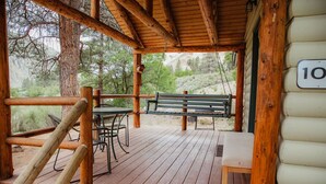 A wooden deck with a table and chairs, a bench, and a cabin number sign. - C-101) The Bluebird Cabin (Sevier)