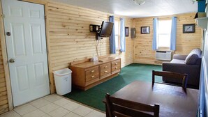 Una stanza con una parete in legno, una televisione fissata al muro, un divano, un tavolo e un cestino.