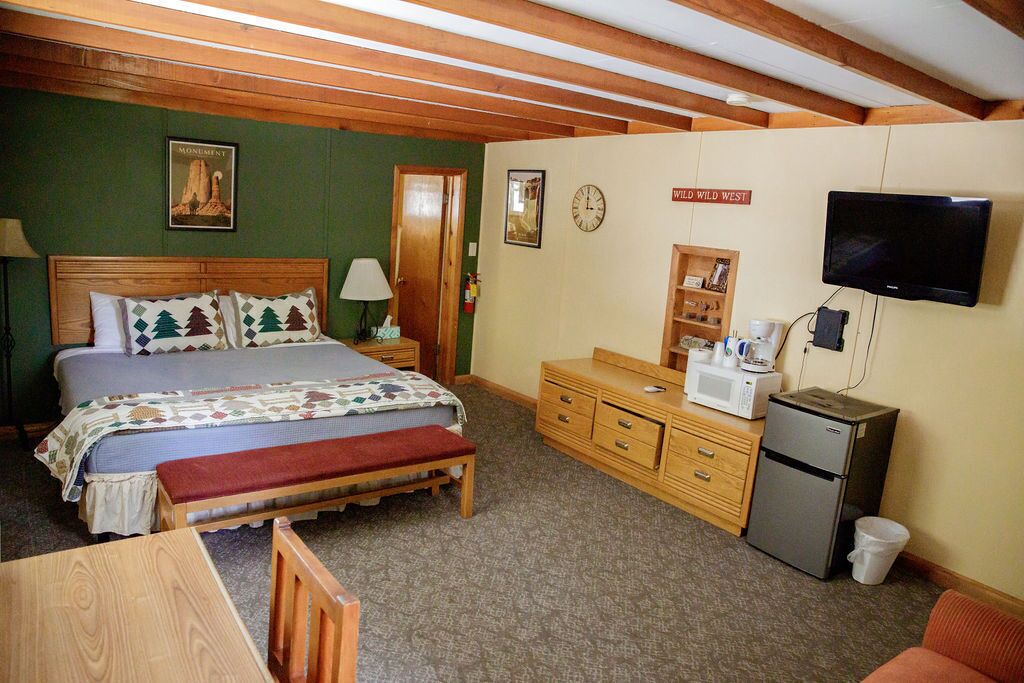 Une chambre à coucher comprenant un lit, un banc en bois, une commode, un four à micro-ondes, un réfrigérateur, un téléviseur et une horloge.