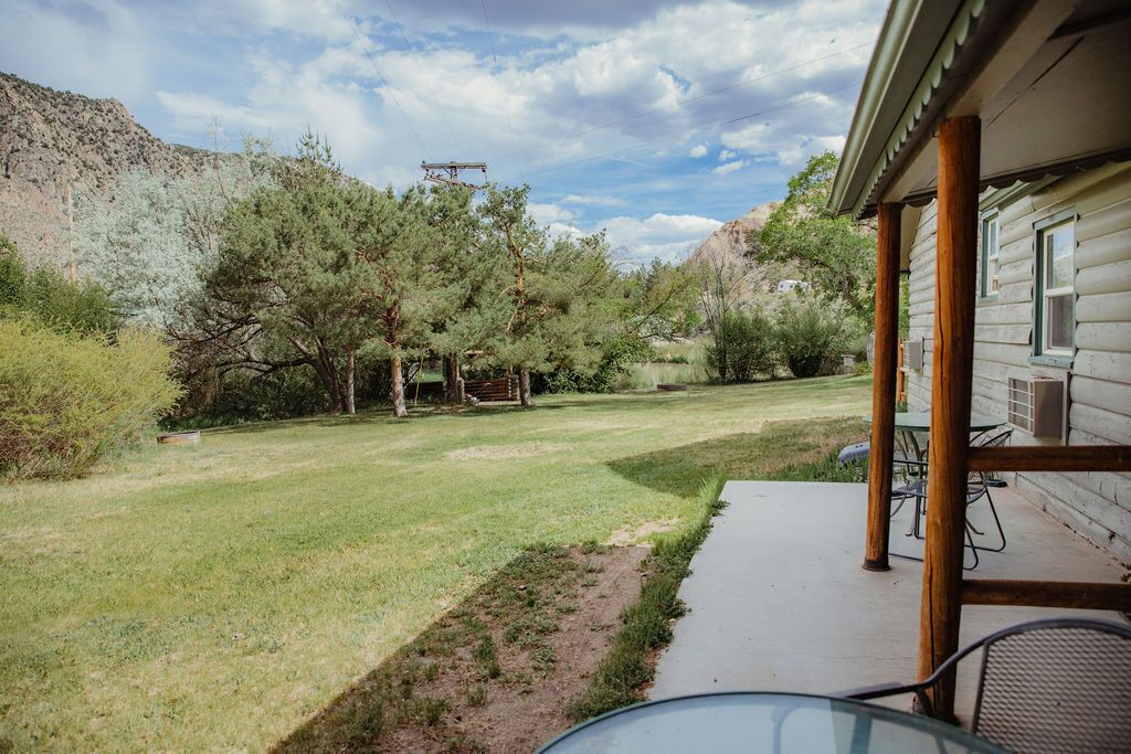 Una cabaña de madera con un porche, un patio cubierto de césped y montañas al fondo.