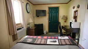 A hotel room with a bed, a desk, a television, a door, and a window with curtains. - C-105) Coyote Gulch Cabin (Sevier)