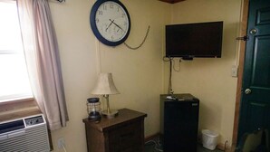 A small room with a wall clock, a television, a heater, a lamp, and a trash bin. - C-105) Coyote Gulch Cabin (Sevier)