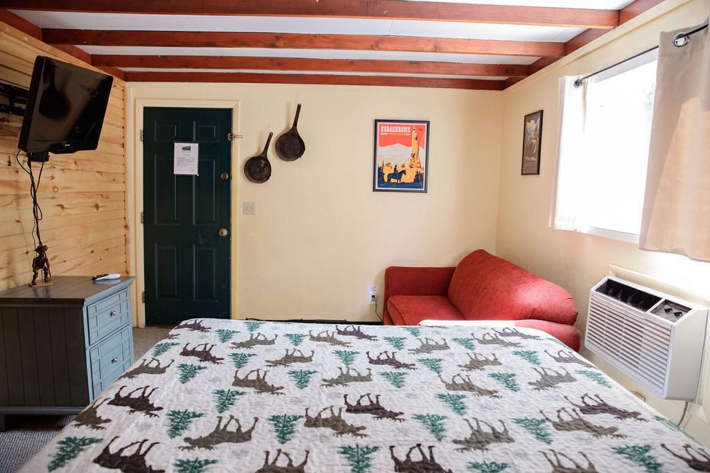 Una habitación con una cama, un sofá rojo, un aparador de madera, un televisor montado en la pared, una puerta y un cartel en la pared.
