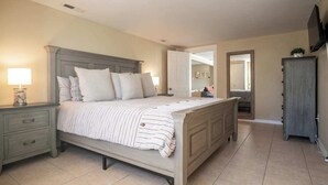 A bedroom with a large bed, a nightstand with a lamp, a dresser, and a mirror.