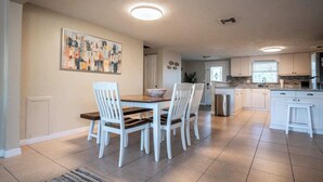 A spacious kitchen with white cabinets, a dining area with a wooden table and white chairs, and a large abstract painting on the wall.