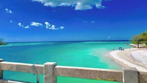 Une plage avec une eau turquoise et limpide, un rivage sablonneux et une clôture en bois au premier plan.