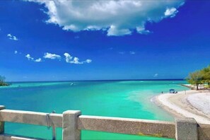 A beach with clear turquoise water, a sandy shore, and a wooden fence in the foreground.