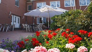 A brick building with outdoor seating and a garden with red and pink flowers. - Gasthaus Heiko Sieb (Wischhafen)