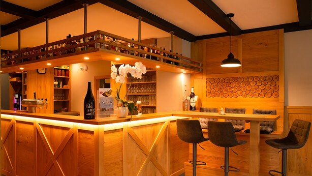 A bar area with wooden bar counter, two bar stools, and a shelf with bottles and glasses. - Gasthaus Heiko Sieb (Wischhafen)