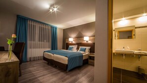 A hotel room with a bed, bedside tables, a desk with a vase, and a bathroom with a sink and mirror. - Gasthaus Heiko Sieb (Wischhafen)