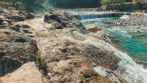 Een natuurlandschap met een waterval, rotsachtig terrein en een gebouw op de achtergrond.