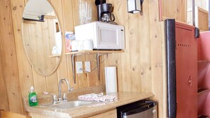 A compact kitchen with wooden walls, a stainless steel dishwasher, a microwave, and a small sink.