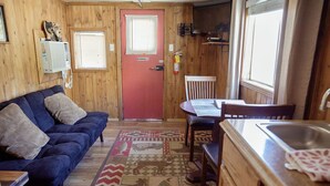 A cozy cabin interior with a red door, a blue sofa, a dining table, and a kitchen area with a sink and stove.