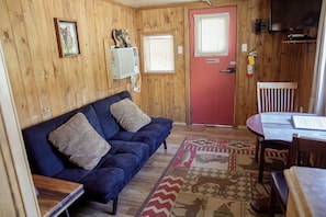 A cozy room with a blue sofa, a red door, a small table, and a patterned rug.