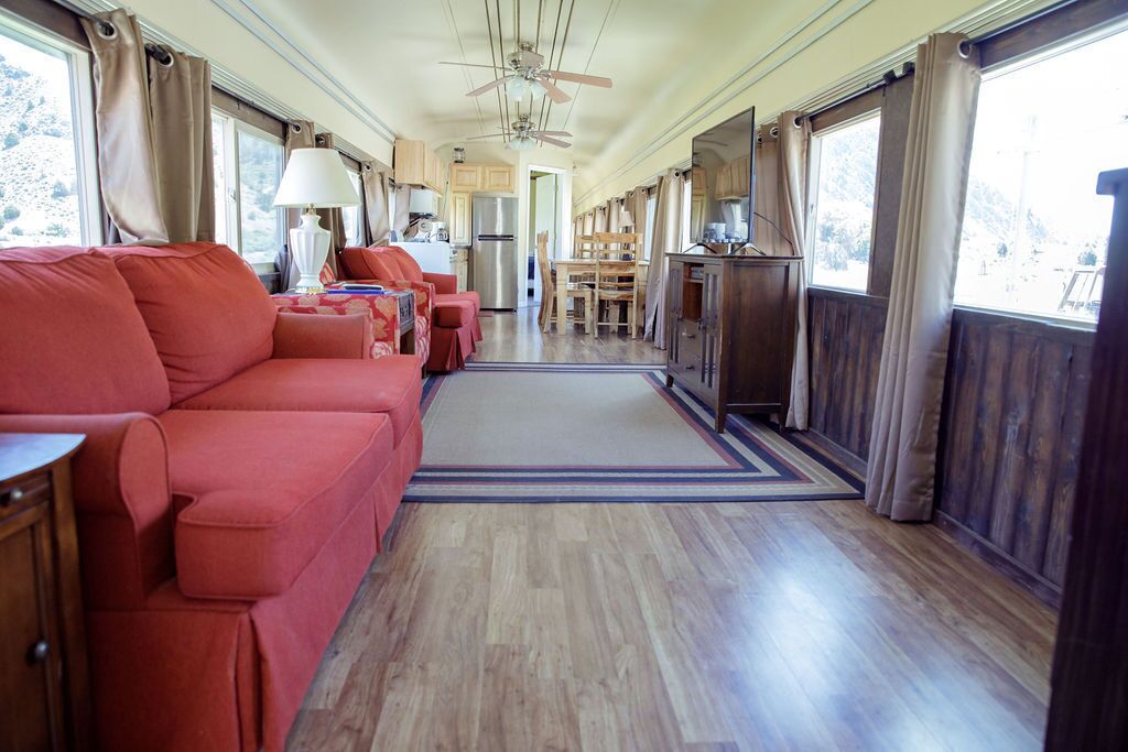 Un interior acogedor con un sofá rojo, suelo de madera, un ventilador de techo y ventanas grandes.