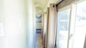 Un couloir étroit au plancher de bois, avec une fenêtre sur le côté droit et une porte au fond.