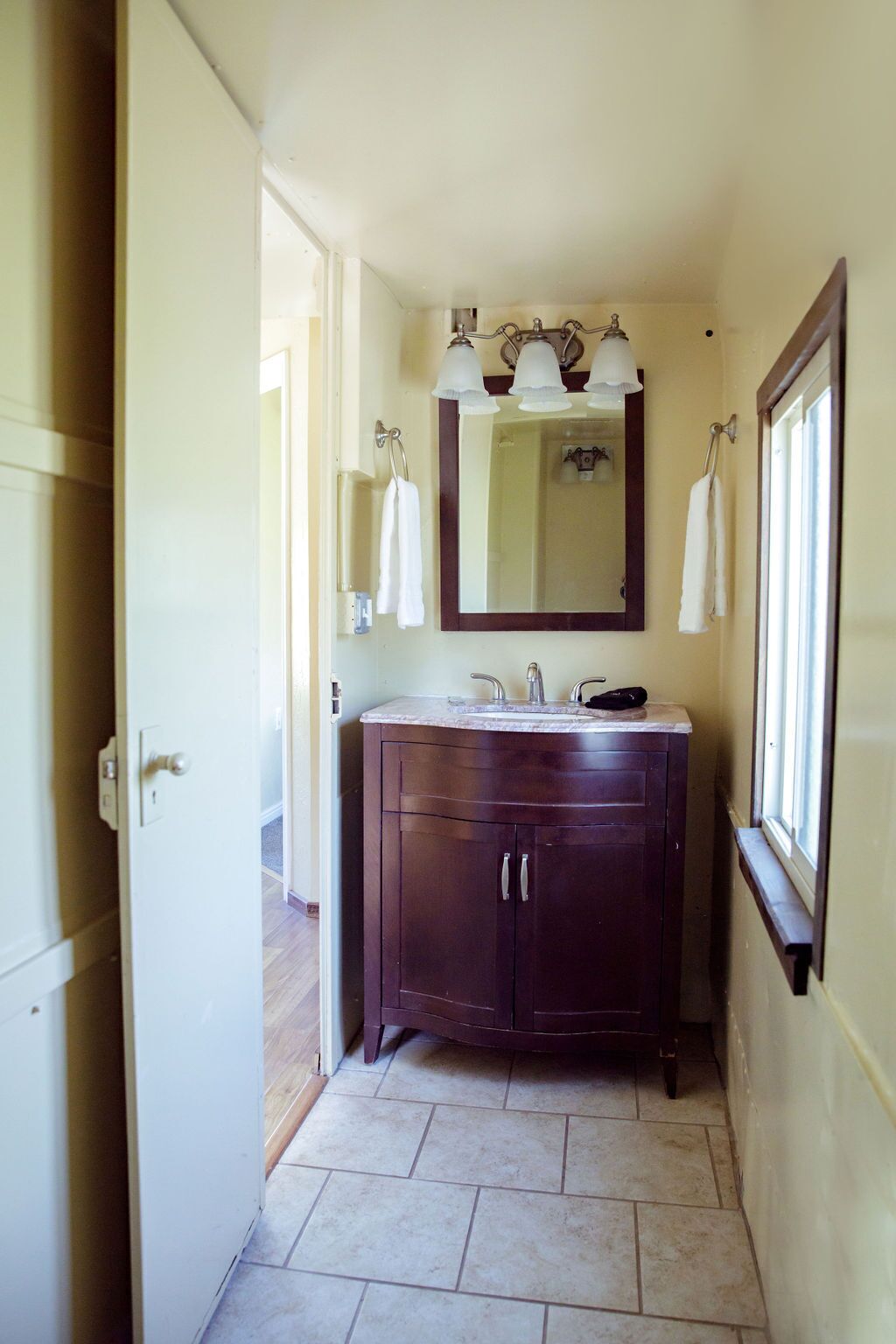 Une salle de bain avec un meuble-lavabo en bois foncé, un grand miroir et trois appliques murales.