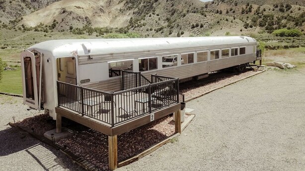 Un wagon de train immobile, doté d’une section avant couverte et d’un quai muni d’une rambarde.