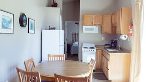 A compact kitchen with wooden cabinets, a microwave, and a stove. There is a dining area with a table and chairs. - T-00003) The Sante Fe (Sevier)