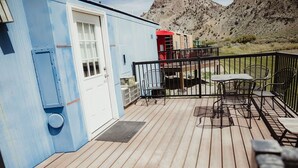 A deck with a table and chairs, a door, and a small outdoor area with a view of a mountainous landscape.