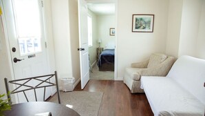 A room with a white sofa, a small table with a remote control, a chair, and a door with a 'No Smoking' sign.