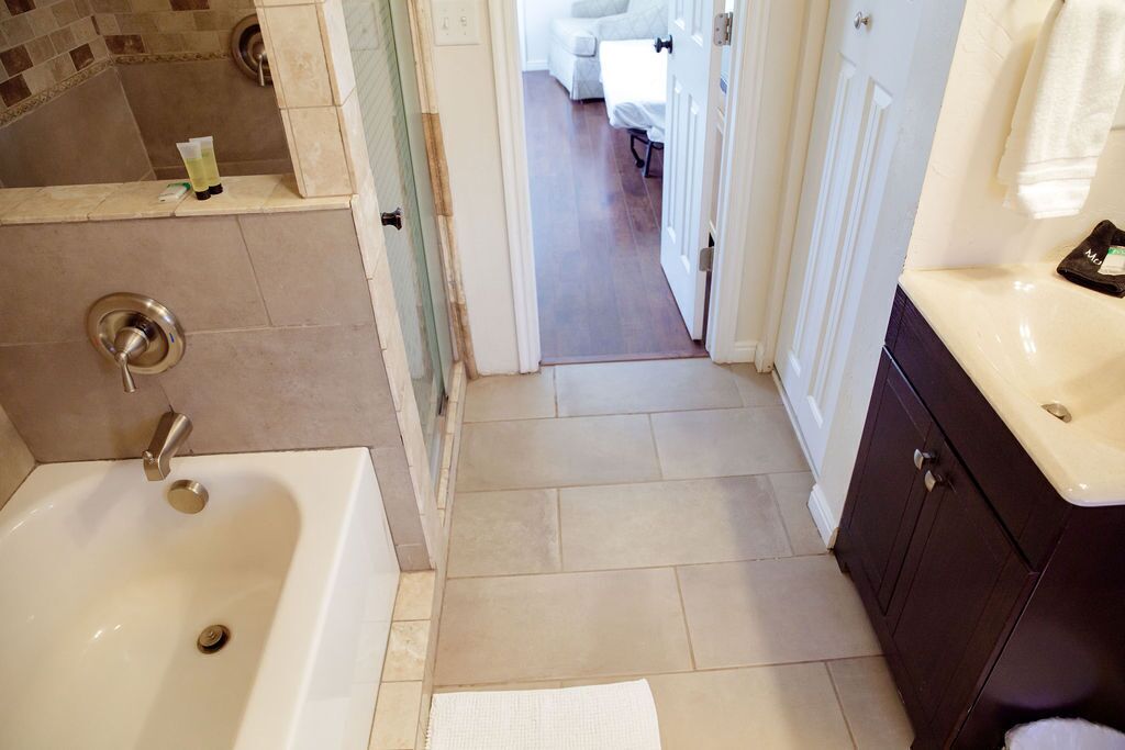 A bathroom with a bathtub, a sink, and a mirror. There is a towel rack and a small shelf with toiletries. The floor is tiled, and the walls are tiled with a mosaic pattern.
