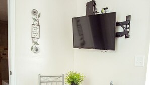 A small dining area with a round table, two chairs, a potted plant, and a mounted TV.