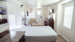 A compact hotel room with a bed, a desk, a chair, and a small kitchenette. - T-0001) Missouri Pacific (Sevier)