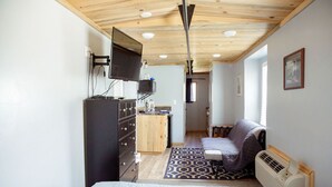 A compact room with a bed, a desk, a chair, a radiator, and a television mounted on the wall. - T-008) The Cotton Belt (Sevier)