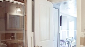 A bathroom with a glass shower enclosure, a white door, and a tiled floor. - T-09) Southern Pacific (Sevier)