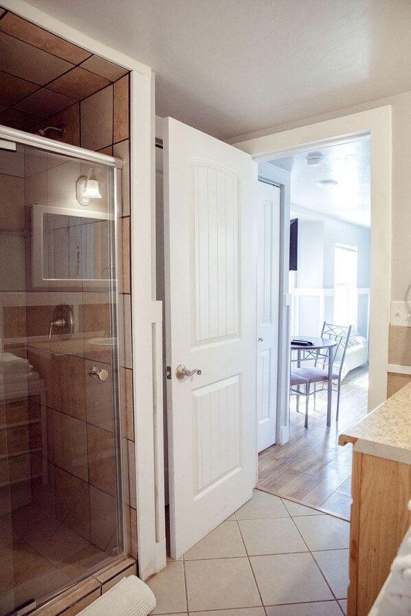 Bathroom features a glass shower enclosure and a door leading to a dining area with a table and chairs.