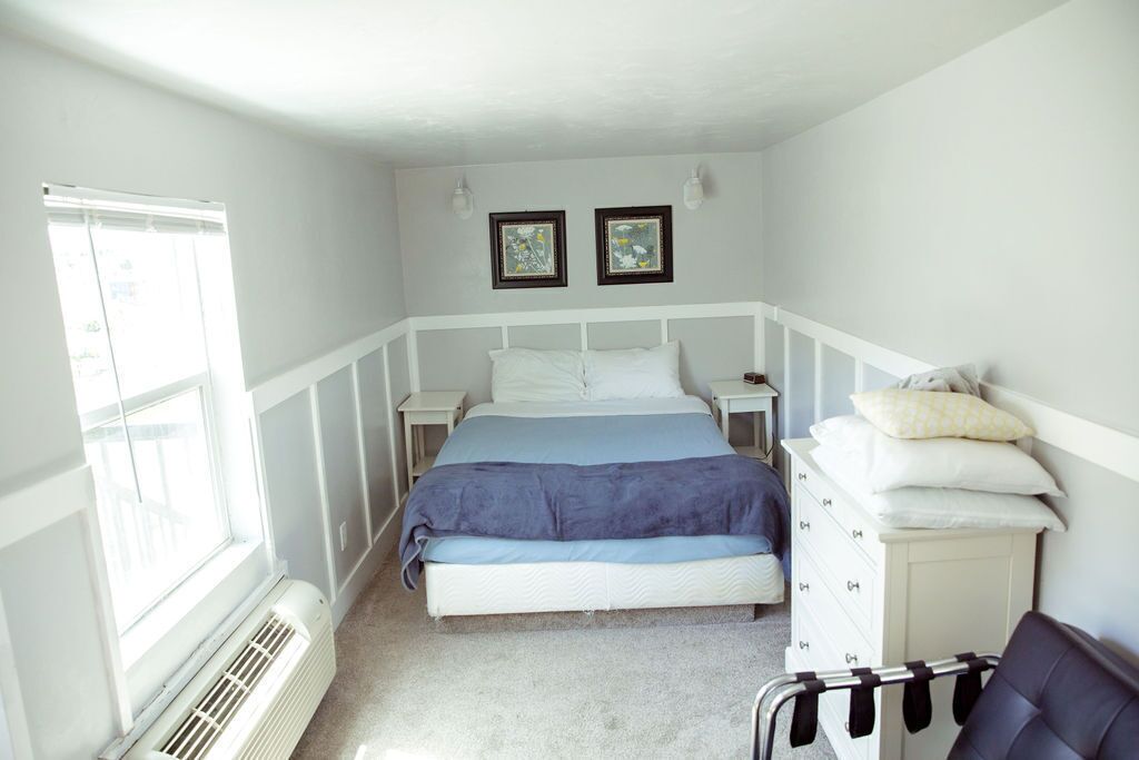 Un dormitorio con cama, mesitas de noche, cómoda y ventana.