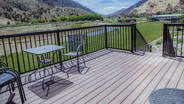 A deck with a table and chairs, overlooking a mountainous landscape and a train in the distance. - T-09) Southern Pacific (Sevier)