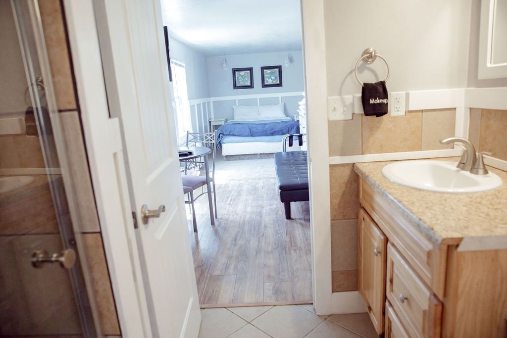 Une chambre d’hôtel comprenant un lit, une petite table, une chaise, une salle de bain avec un lavabo et un espace douche.