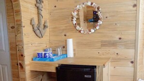 A compact kitchenette with a black refrigerator, wooden shelves, a small stool, and a mirror with a seashell border. - T-10) Northern Pacific (Sevier)
