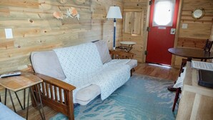 A cozy cabin interior with a wooden floor, a sofa, a small table, and a red door. - T-10) Northern Pacific (Sevier)