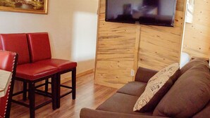 A living room with a wooden wall panel, a flat-screen TV, a red leather sofa, a brown sofa, and a wooden coffee table. - T-11) Great Northern (Sevier)
