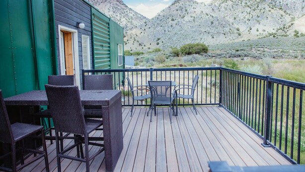A deck with outdoor furniture, a green building, and a mountainous landscape in the background. - T-11) Great Northern (Sevier)