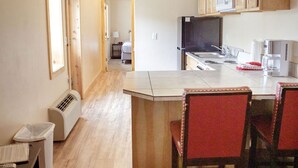 A compact kitchen with wooden cabinets, a microwave, and a refrigerator. There is a small dining area with a table and chairs. - T-11) Great Northern (Sevier)