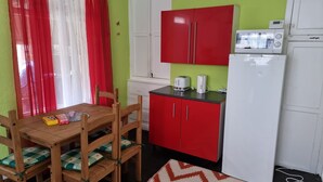 Una cocina funcional con armarios rojos, un refrigerador blanco y un microondas. Hay una mesa de comedor de madera con sillas y un tapete en el suelo.
