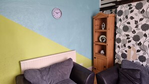 Una habitación con una cama, un armario de madera con objetos decorativos, un reloj en la pared y una cortina estampada con motivos florales.