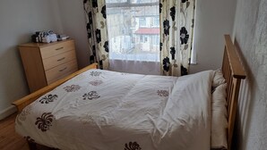 Un dormitorio con una cama de madera, un aparador de madera y una ventana con cortinas florales.