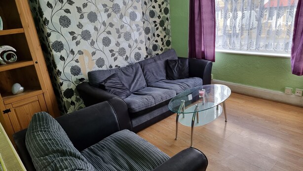 Un salón con un sofá gris, una mesa de centro de cristal y un estante de madera con objetos decorativos.