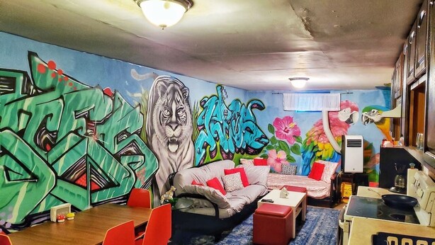 Ein Zimmer mit Wandgemälde, einer Couch, einem Esstisch mit Stühlen und einer Küchenzeile.
